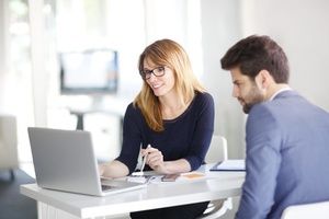 Portrait of investment advisor businesswoman sitting at office in front of computer and consulting with young professional man.