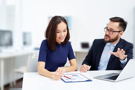 Photo of man and woman at desk with computer and paper documents